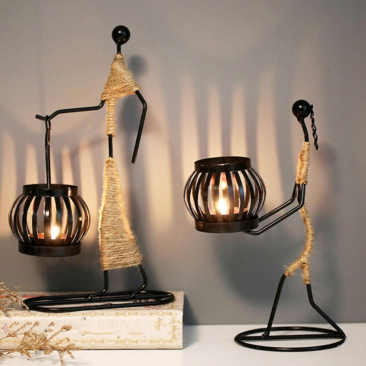 Handcrafted tribal lady metal candle holder with jute wrapping and matte black finish, holding a flickering tea light candle on a rustic wooden table