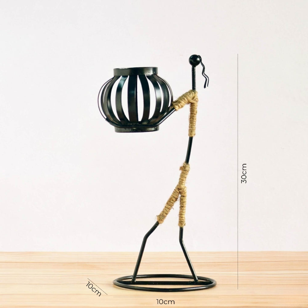 Handcrafted tribal lady metal candle holder with jute wrapping and matte black finish, holding a flickering tea light candle on a rustic wooden table