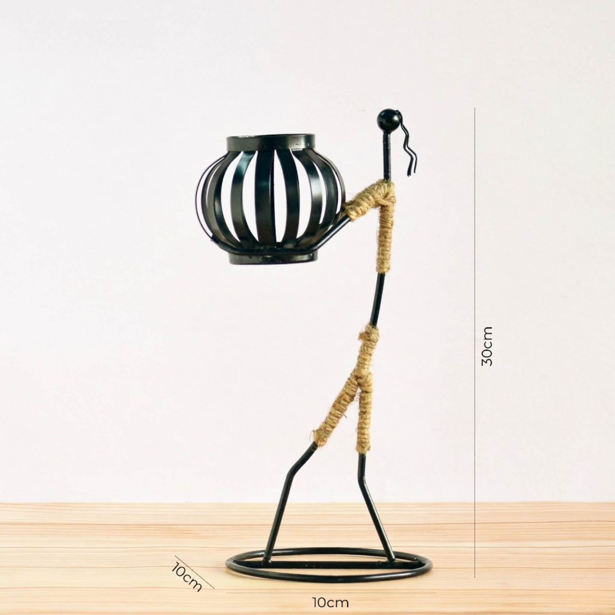 Handcrafted tribal lady metal candle holder with jute wrapping and matte black finish, holding a flickering tea light candle on a rustic wooden table
