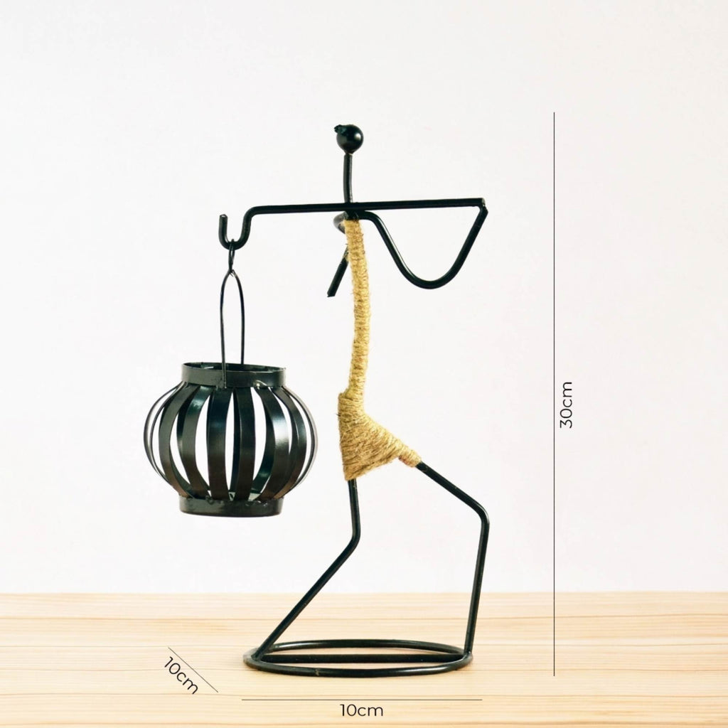 Handcrafted tribal lady metal candle holder with jute wrapping and matte black finish, holding a flickering tea light candle on a rustic wooden table