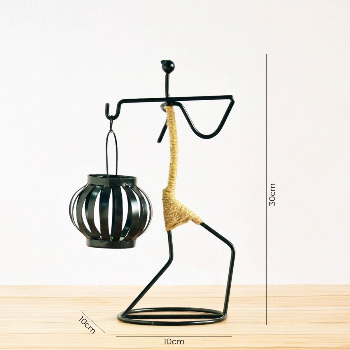 Handcrafted tribal lady metal candle holder with jute wrapping and matte black finish, holding a flickering tea light candle on a rustic wooden table