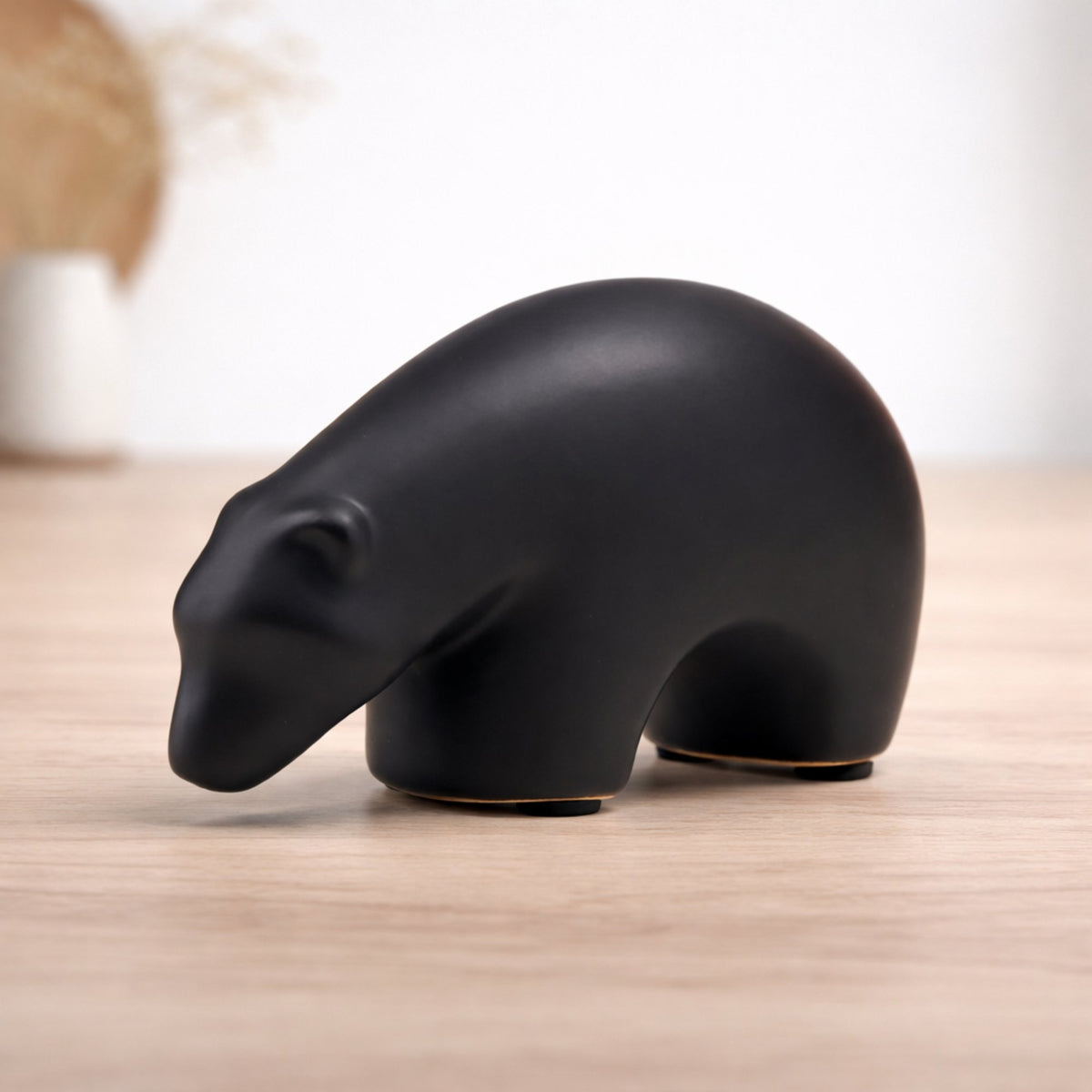 Minimalist matte black ceramic bear sculpture set on wooden surface 