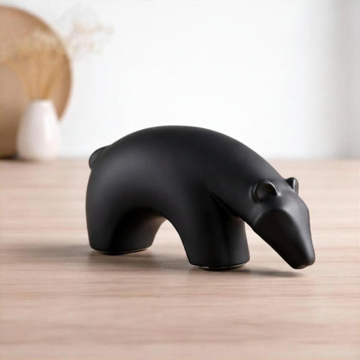 Minimalist matte black ceramic bear sculpture set on wooden surface with modern lifestyle background