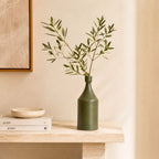 Luxury ceramic bottle-shaped vase with matte finish styled on a beige travertine console table in a modern Scandinavian-inspired interior with olive branches and minimalist décor.