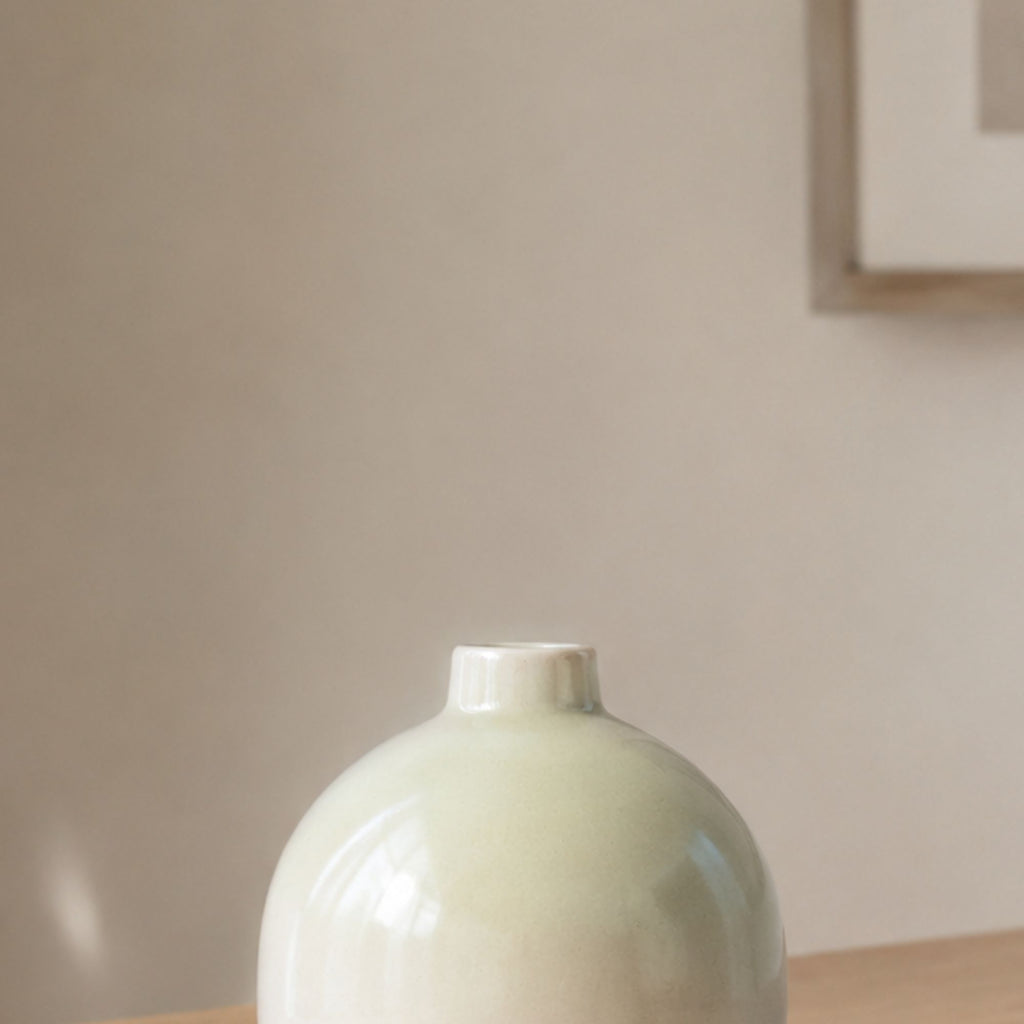Luxury round ceramic flower vase in minimalist modern design held in hand against vibrant pink background for premium home décor and office styling.