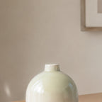 Luxury round ceramic flower vase in minimalist modern design held in hand against vibrant pink background for premium home décor and office styling.