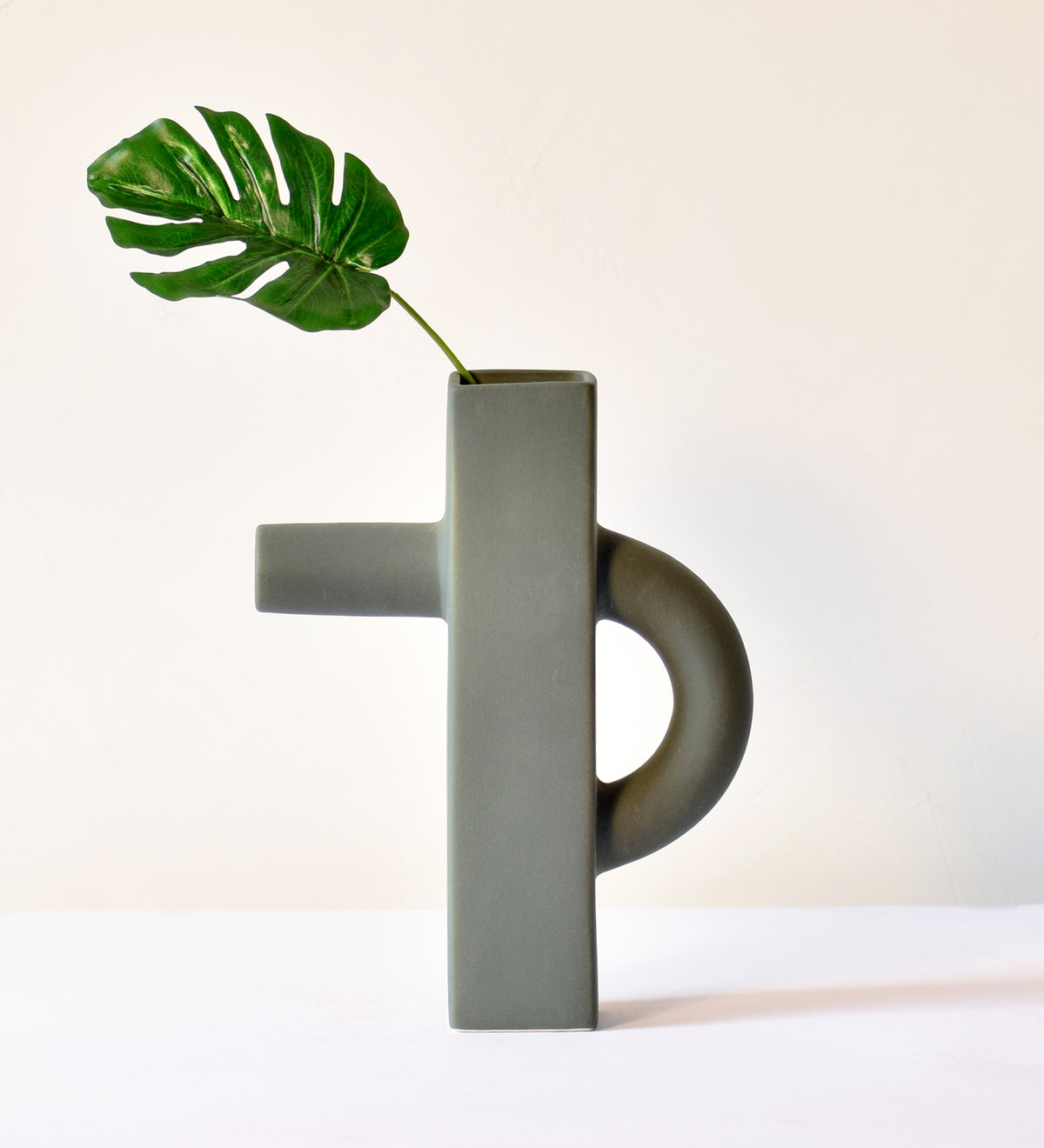 Modern sculptural ceramic flower vase with matte sage green finish styled with tropical leaf in a contemporary luxury interior setting.