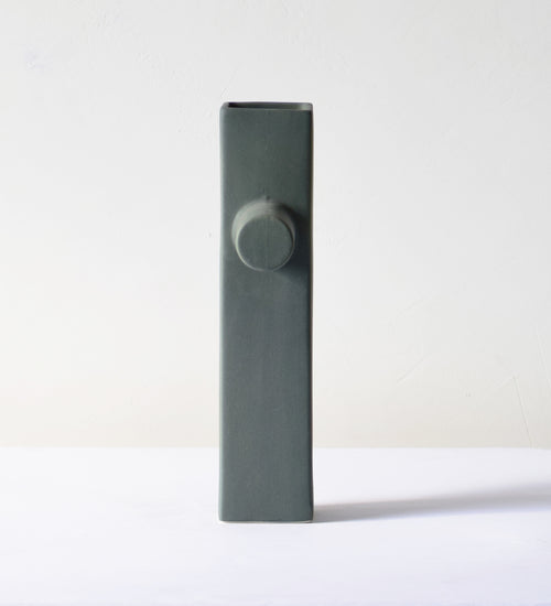 Modern sculptural ceramic flower vase with matte sage green finish styled with tropical leaf in a contemporary luxury interior setting.