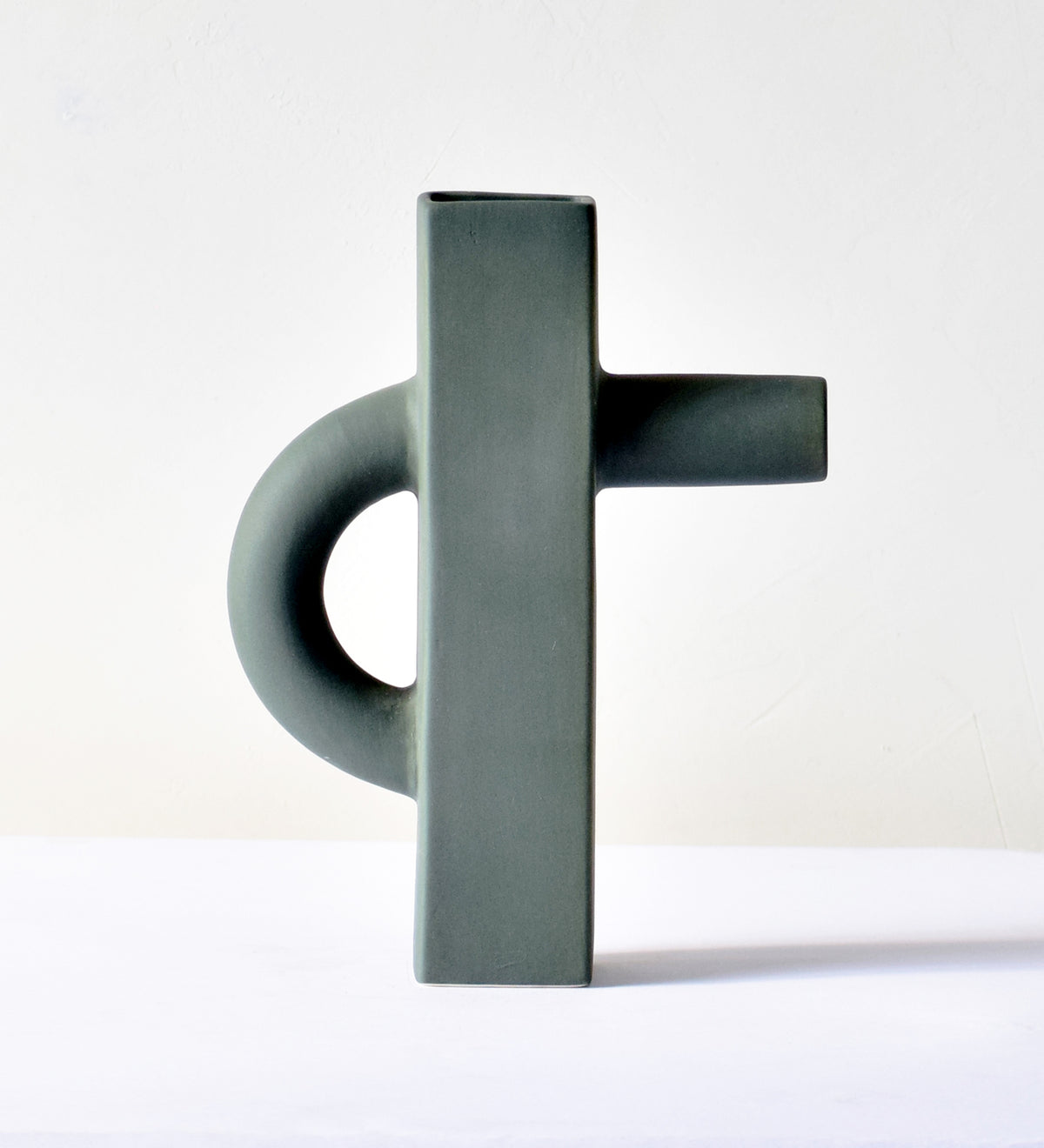 Modern sculptural ceramic flower vase with matte sage green finish styled with tropical leaf in a contemporary luxury interior setting.