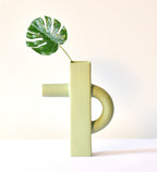 Modern sculptural ceramic flower vase with matte sage green finish styled with tropical leaf in a contemporary luxury interior setting.