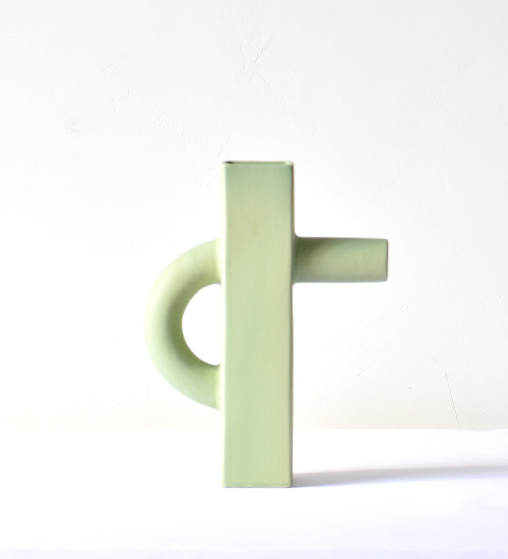 Modern sculptural ceramic flower vase with matte sage green finish styled with tropical leaf in a contemporary luxury interior setting.