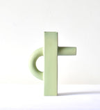 Modern sculptural ceramic flower vase with matte sage green finish styled with tropical leaf in a contemporary luxury interior setting.
