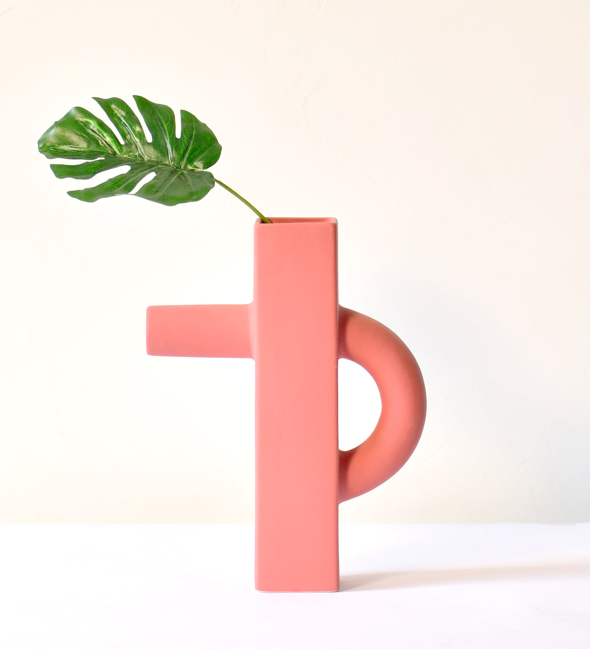 Modern sculptural ceramic flower vase with matte sage green finish styled with tropical leaf in a contemporary luxury interior setting.