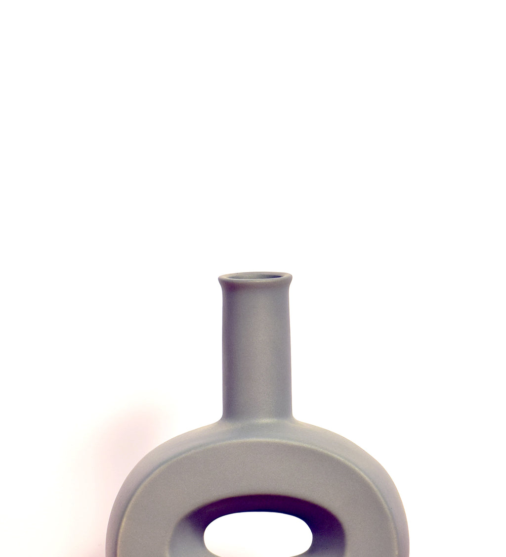 Modern hollow flat ceramic vase with sculptural circular design styled on a console table in a contemporary luxury living room interior.