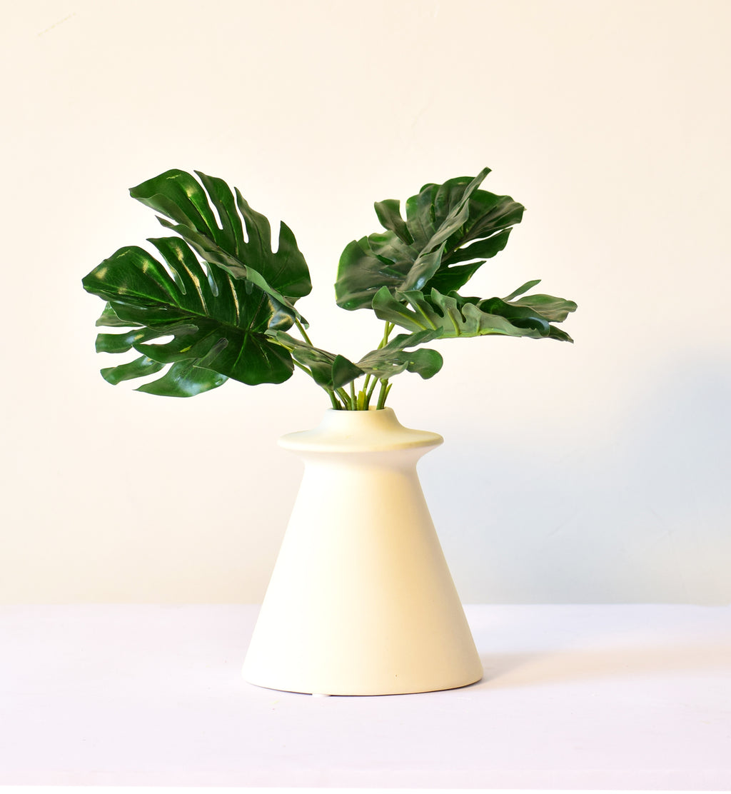 Modern white ceramic flower vase with tropical green monstera leaves on minimal background