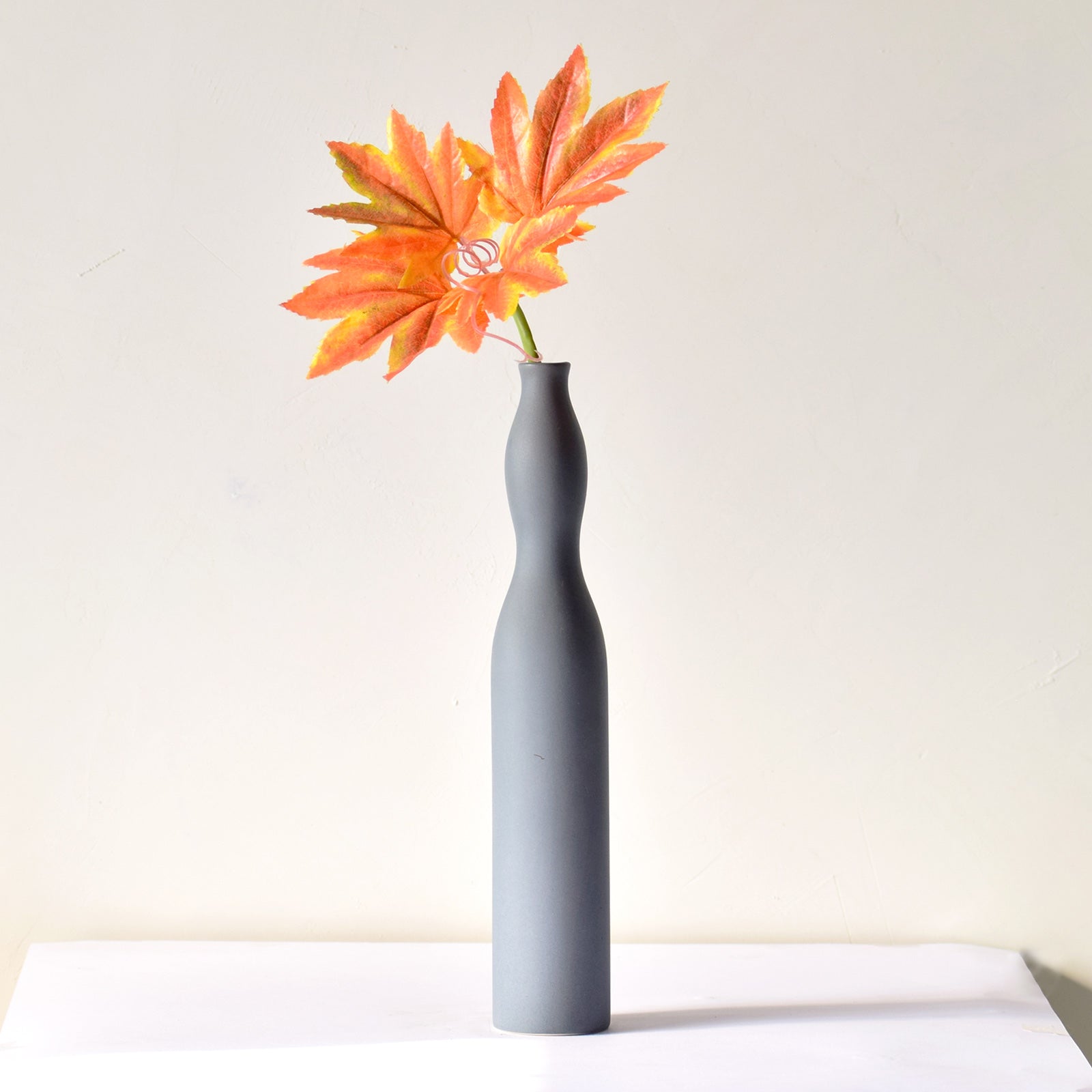 Flute Vase Luxury slim Nordic ceramic flower vase with matte grey finish and orange artificial maple leaves on white table for modern home décor interiors.