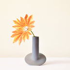 Handmade orbital ceramic flower vase with sculptural modern design styled with flowers in a luxury contemporary living room.
