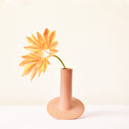 Handmade orbital ceramic flower vase with sculptural modern design styled with flowers in a luxury contemporary living room.