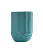 Modern dark green ribbed ceramic flower vase with yellow floral arrangement on minimal beige background