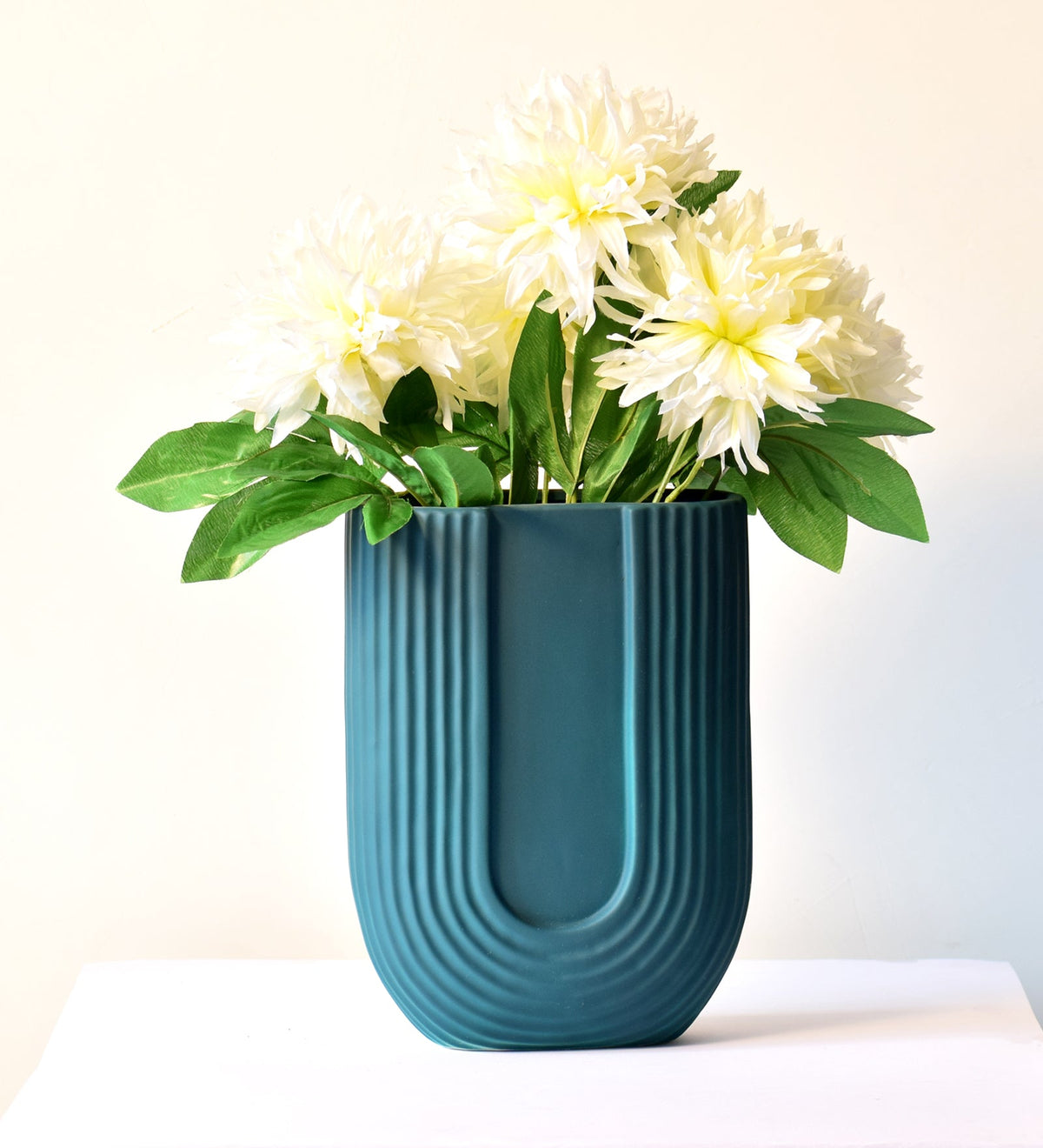 Modern dark green ribbed ceramic flower vase with yellow floral arrangement on minimal beige background