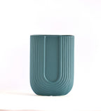 Modern dark green ribbed  u shaped ceramic flower vase with yellow floral arrangement on minimal beige background