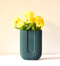 Modern dark green ribbed  u shaped ceramic flower vase with yellow floral arrangement on minimal beige background