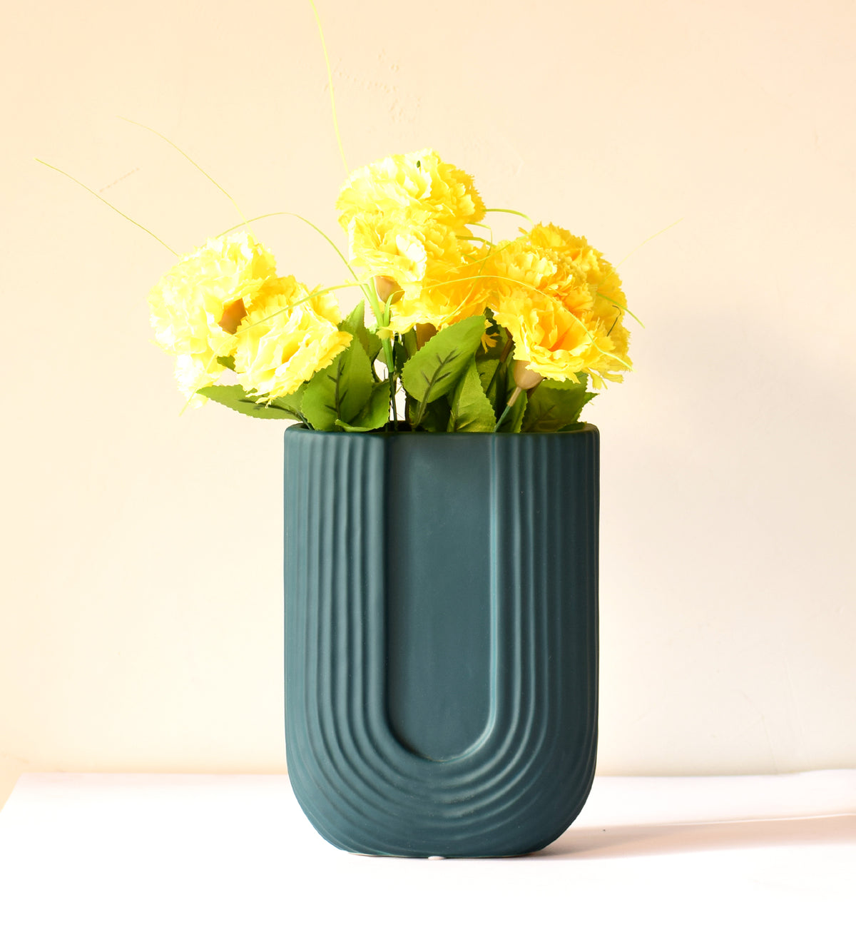 Modern dark green ribbed  u shaped ceramic flower vase with yellow floral arrangement on minimal beige background