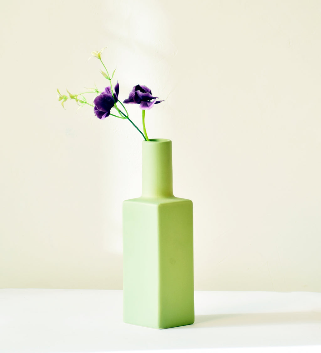 Luxury ceramic bottle-shaped vase with matte finish styled on a beige travertine console table in a modern Scandinavian-inspired interior with olive branches and minimalist décor.