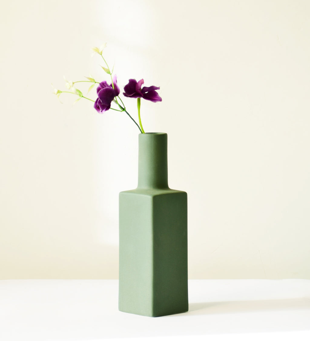 Luxury ceramic bottle-shaped vase with matte finish styled on a beige travertine console table in a modern Scandinavian-inspired interior with olive branches and minimalist décor.