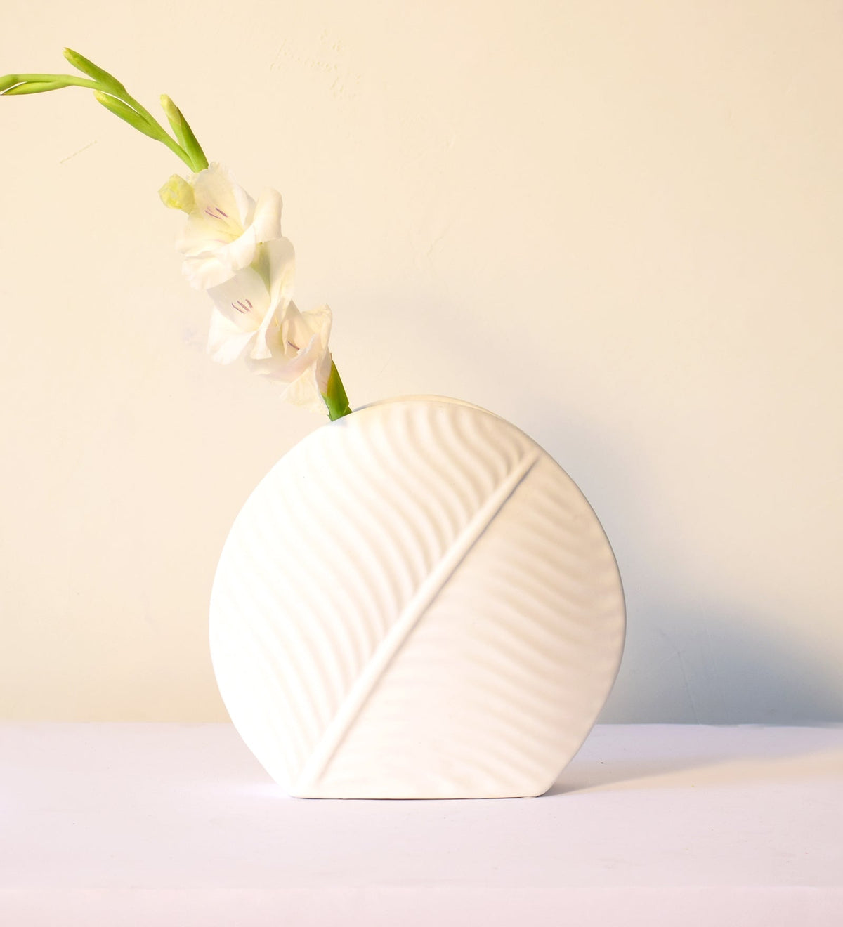 White leaf ceramic flower vase styled with fresh blooms in a modern luxury living room featuring elegant contemporary décor.
