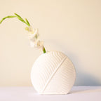White leaf ceramic flower vase styled with fresh blooms in a modern luxury living room featuring elegant contemporary décor.
